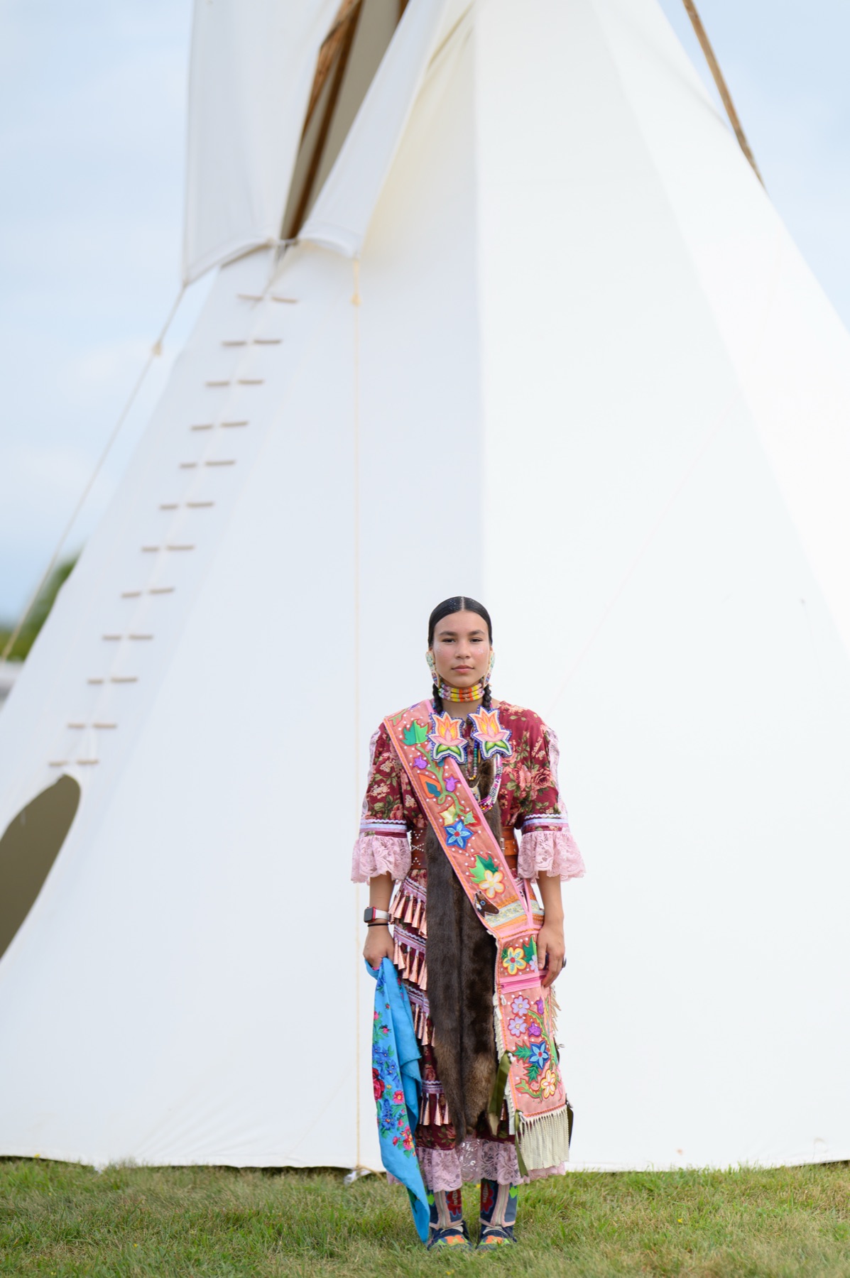 Valerie Leith standing in jingle dress regalia in front of a tipi