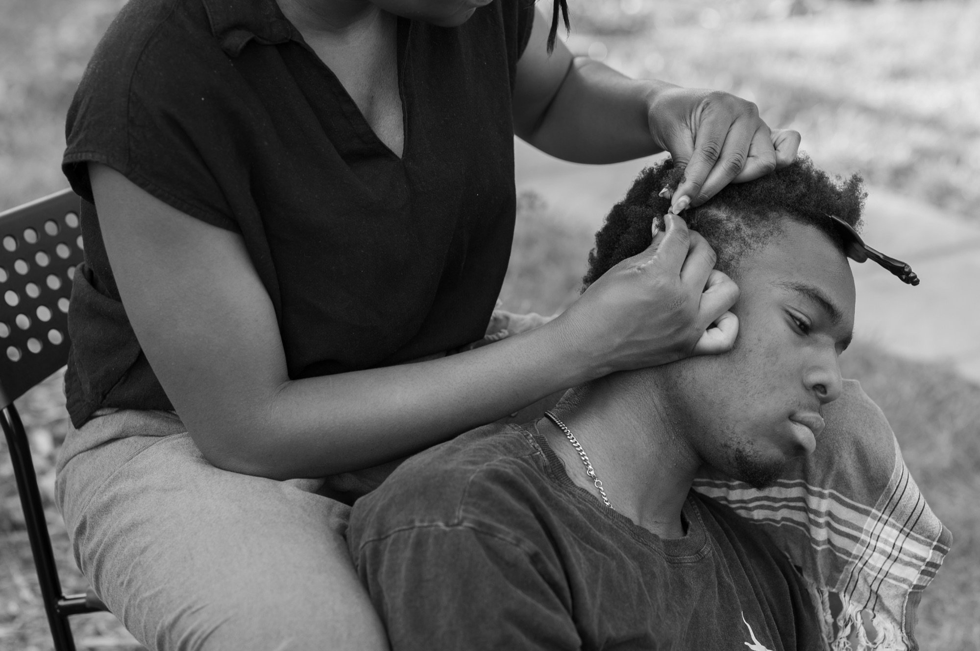 Gideon Wonosikou resting his head against Deino's knee while she parts a section of his hair at the temple