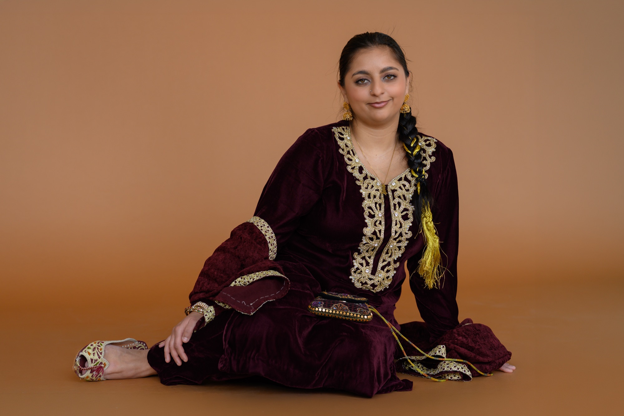 Aliza Mashadi seated in a maroon velvet shalwar kameez with gold embroidery